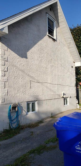 A white stucco house exterior featuring a prominent horizontal crack along the wall and two basement windows.