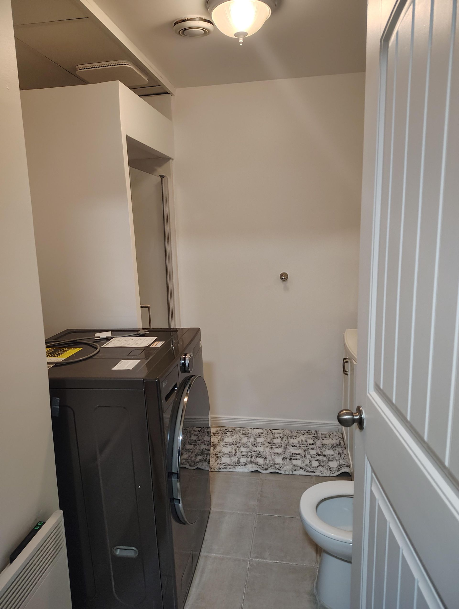 A bathroom interior showing a dark grey front-loading laundry unit on the left and a toilet on the right.
