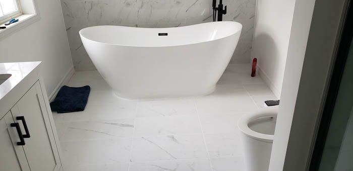 A modern bathroom with white marble-style floors and wall tile, featuring a freestanding white tub and a white toilet.