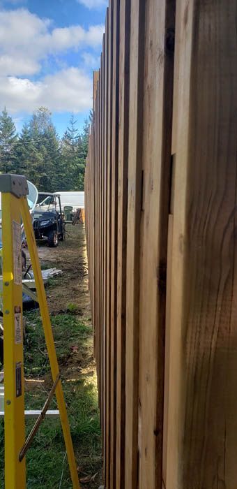 A close-up view of a wooden fence under construction, with a yellow ladder visible in the foreground.