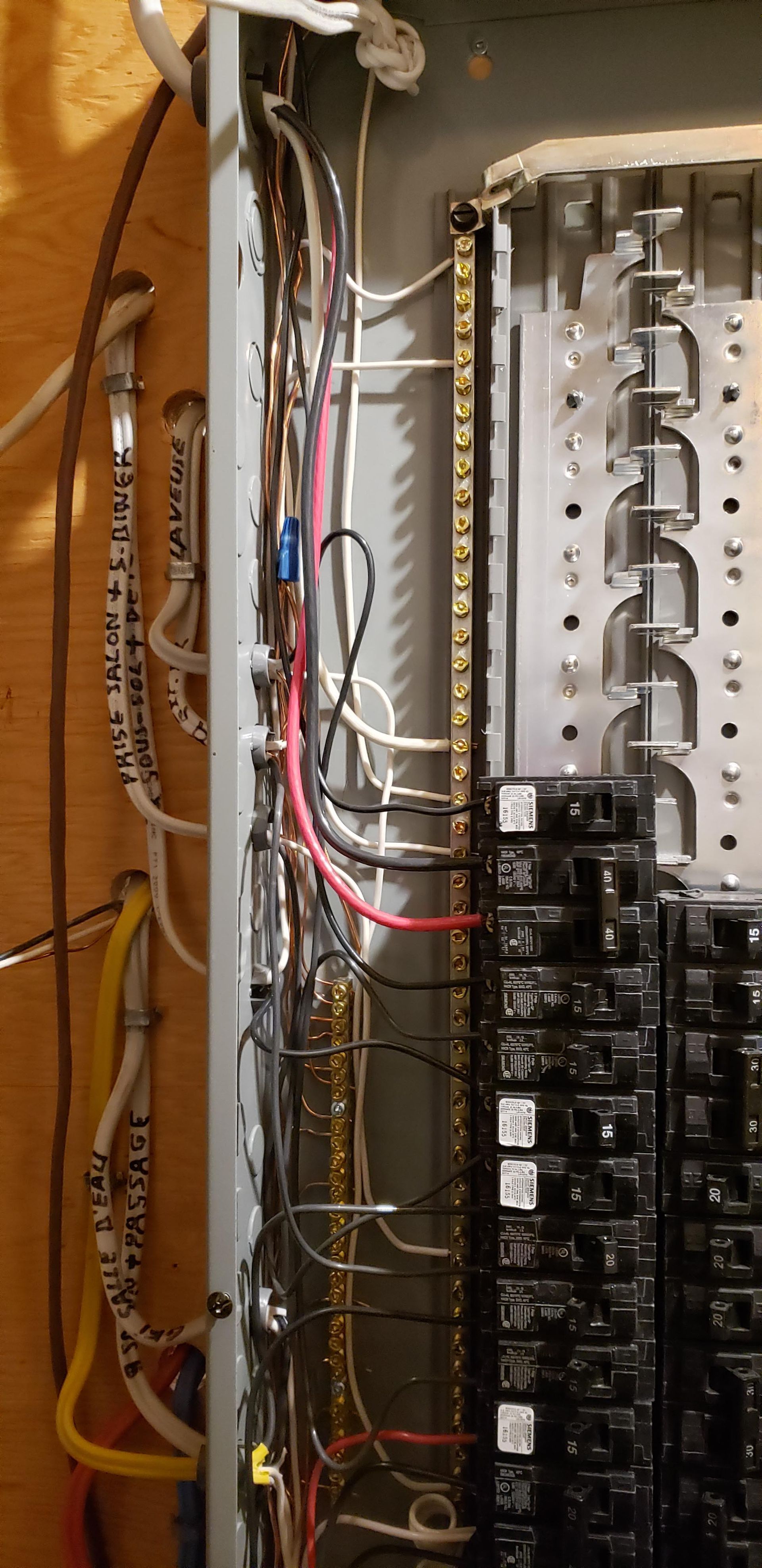 Tableau électrique ouvert montrant les connexions des fils à un bornier et divers disjoncteurs.