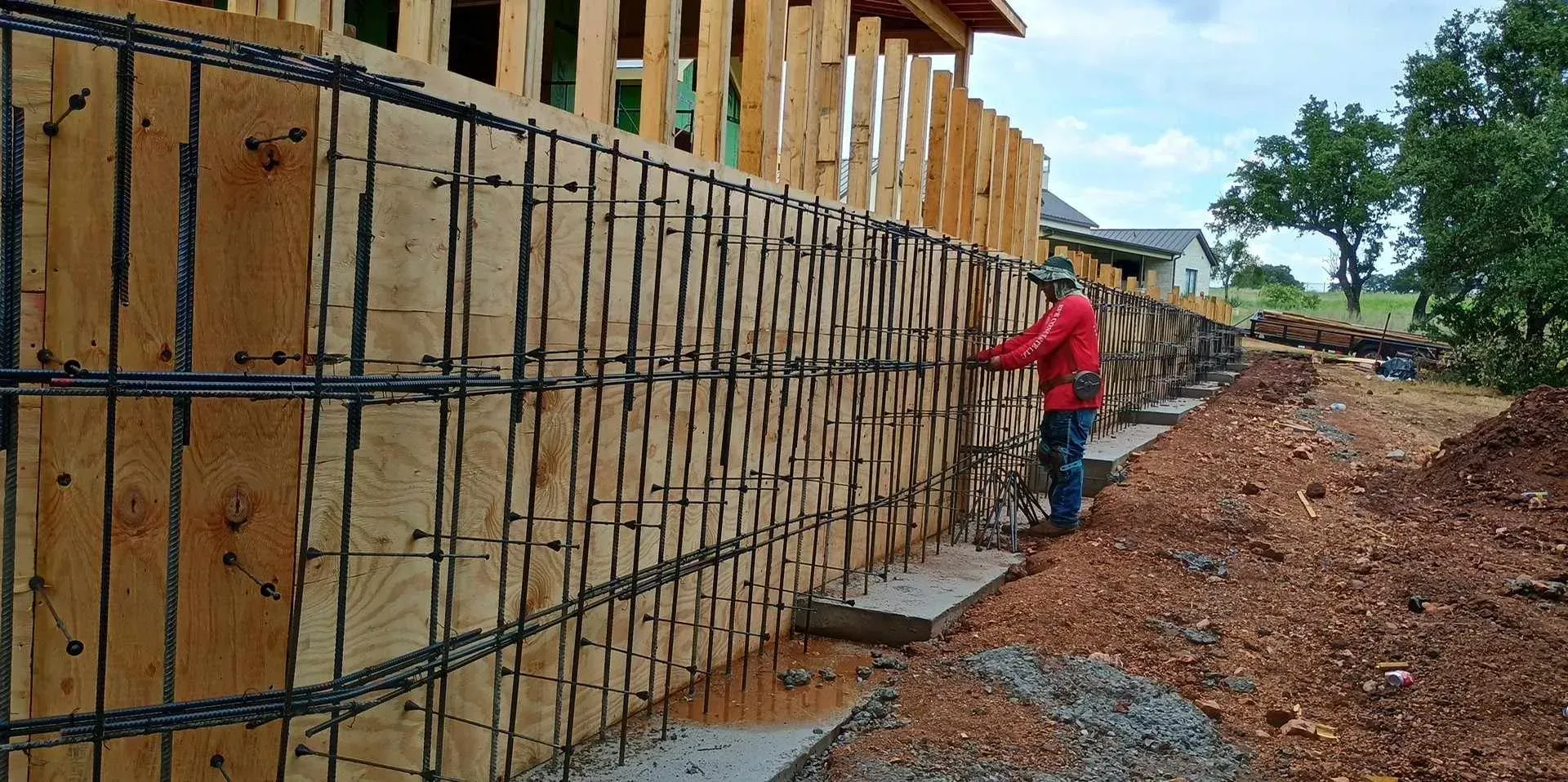 A man in a red jacket is working on a wooden fence.