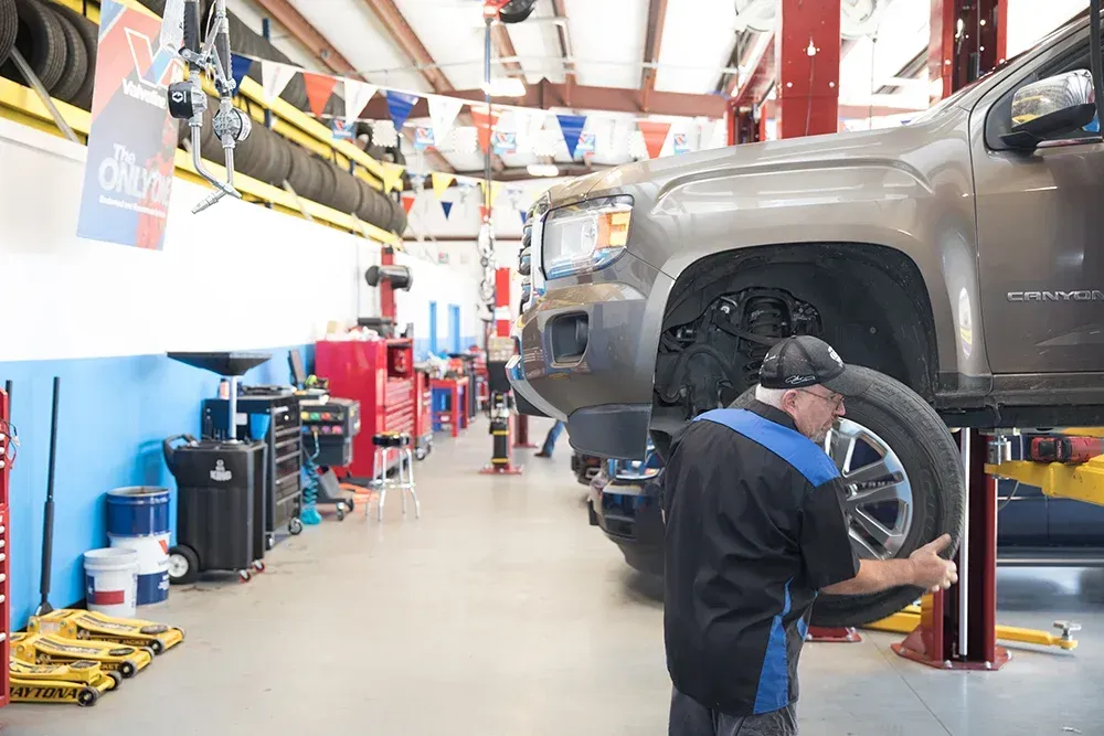 A mechanic in a garage attaches a tire to a raised brown pickup truck.