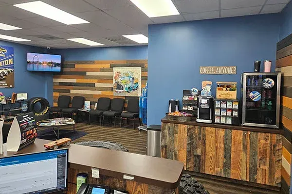 A waiting area at an auto shop with dark chairs, wood-paneled walls, a beverage station, and a reception desk.