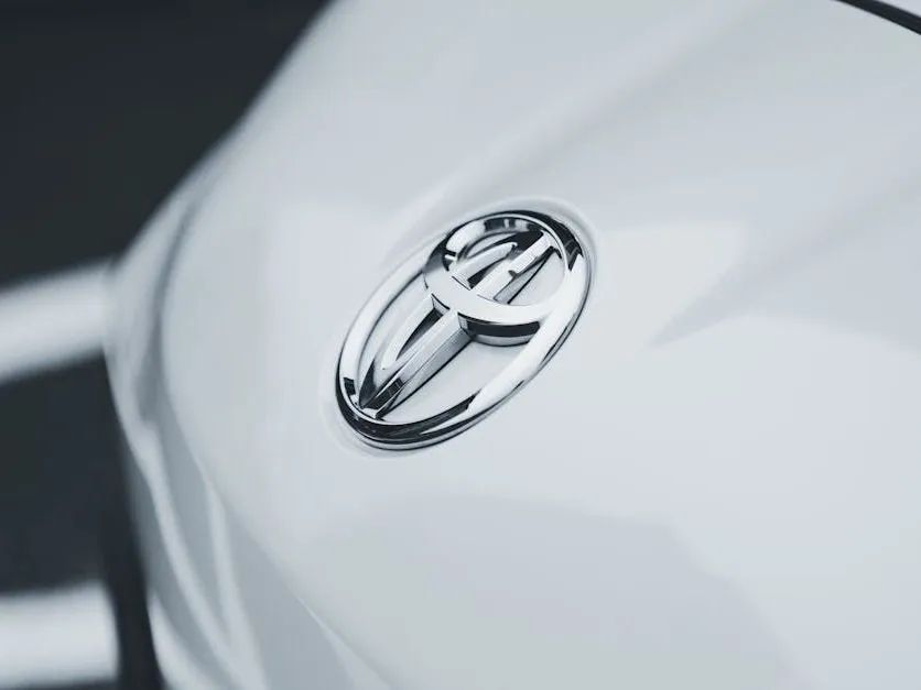 A chrome Toyota logo emblem mounted on the smooth, glossy white surface of a vehicle's hood.