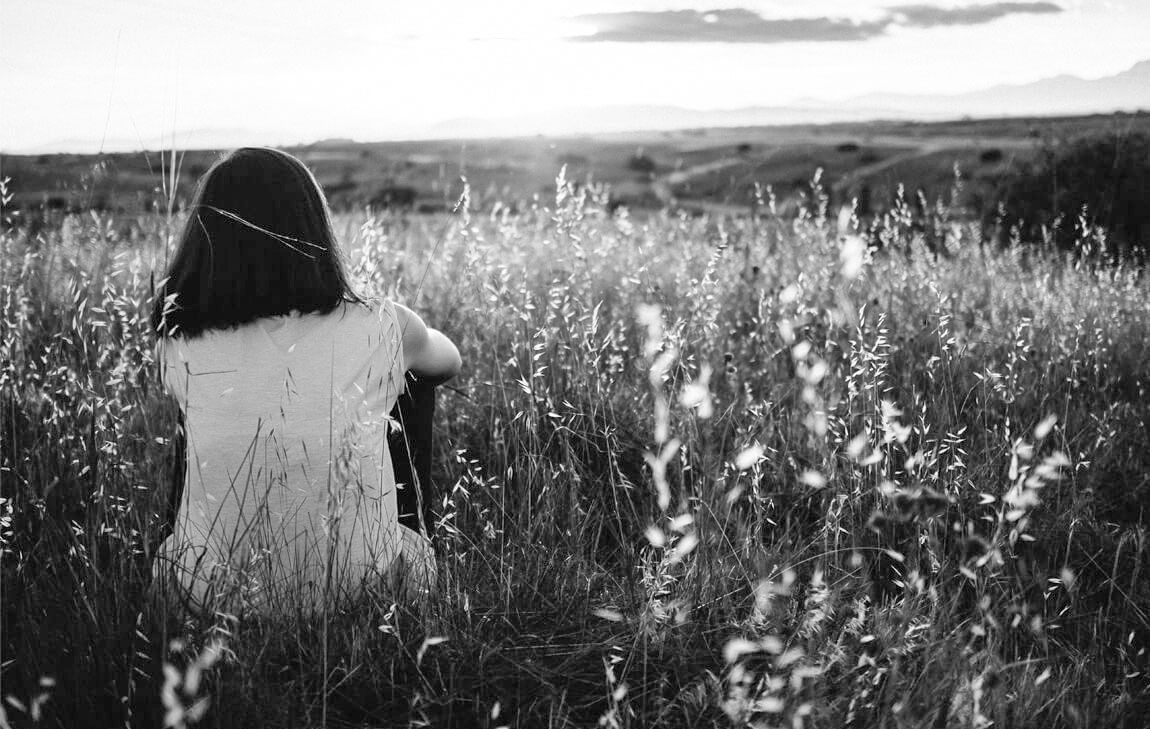 Young girl watching a sunset as she sits in a field of tall grass