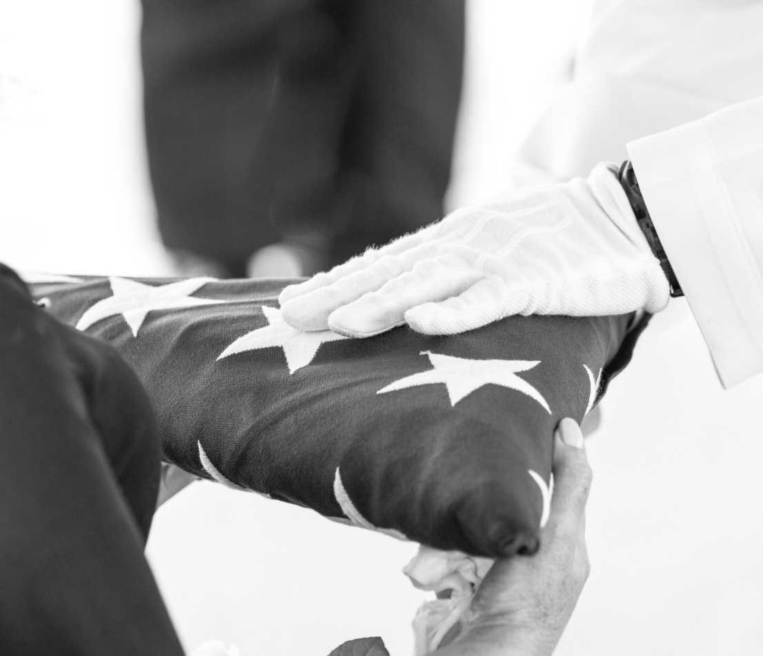 Uniformed officer passing a folded American flag to a family member at a veteran’s funeral