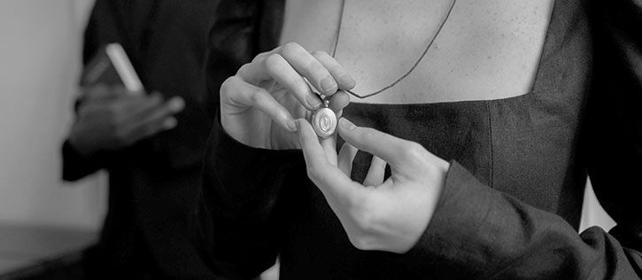 A funeral mourner in a black dress holds a piece of memorial jewelry: a locket containing cremated remains