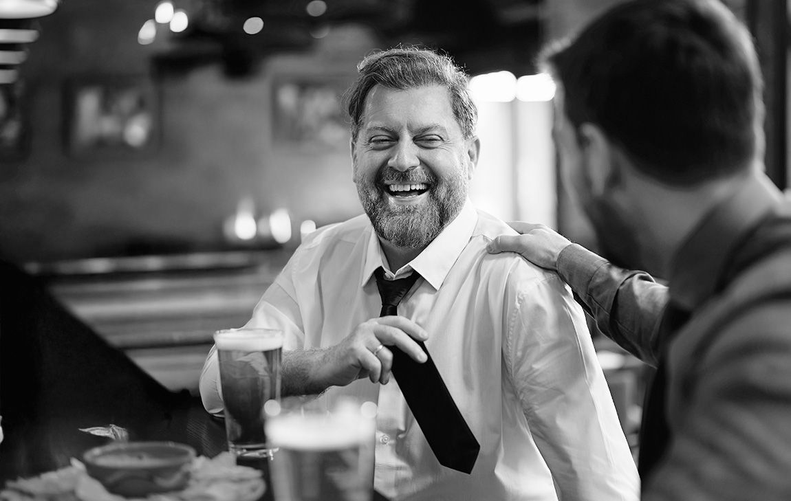Friends sharing stories and laughter over drinks at a funeral gathering, reflecting the supportive, personal atmosphere often found at a non-religious celebration of life.