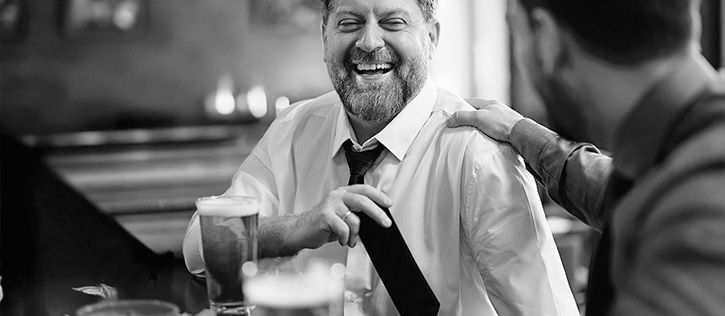 Friends sharing stories and laughter over drinks at a funeral gathering, reflecting the supportive, personal atmosphere often found at a non-religious celebration of life.
