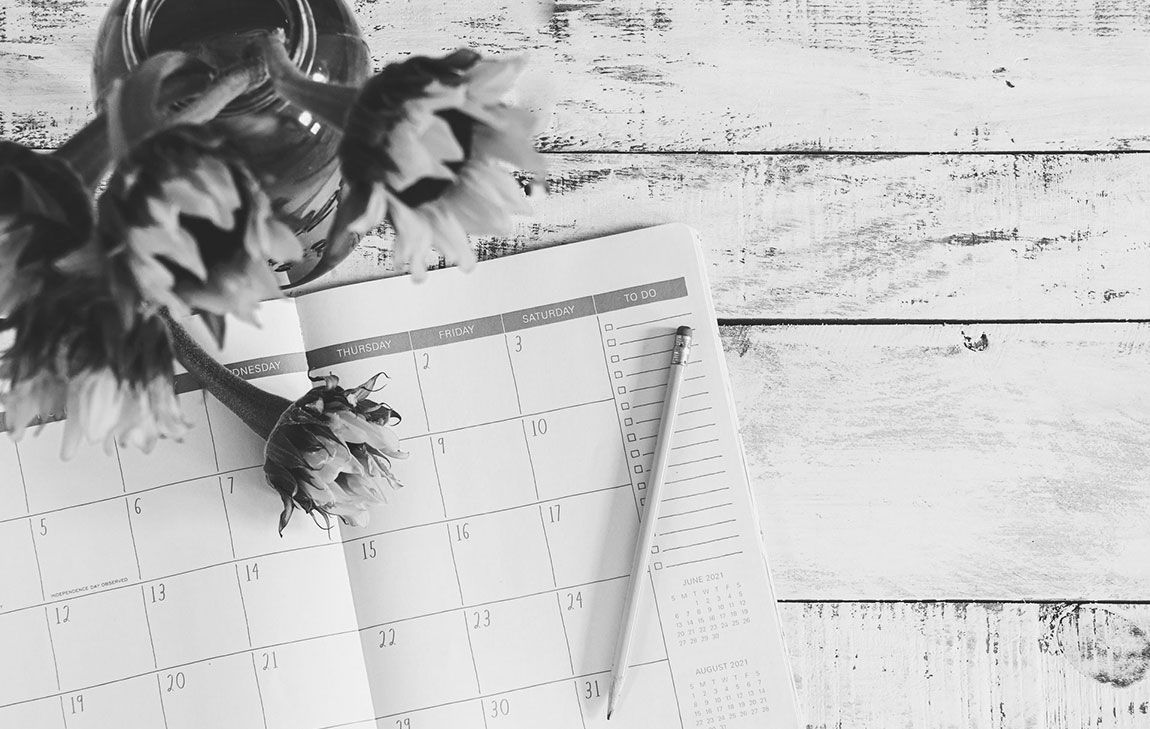 Open calendar with a pencil and flowers, symbolizing the planning involved in funeral arrangements.