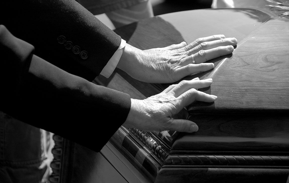 Hands gently resting on a casket during a direct funeral service.