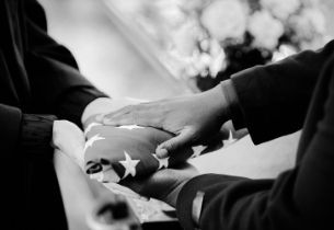 Military honor guard presenting a folded American flag during a veteran funeral service with full military honors.
