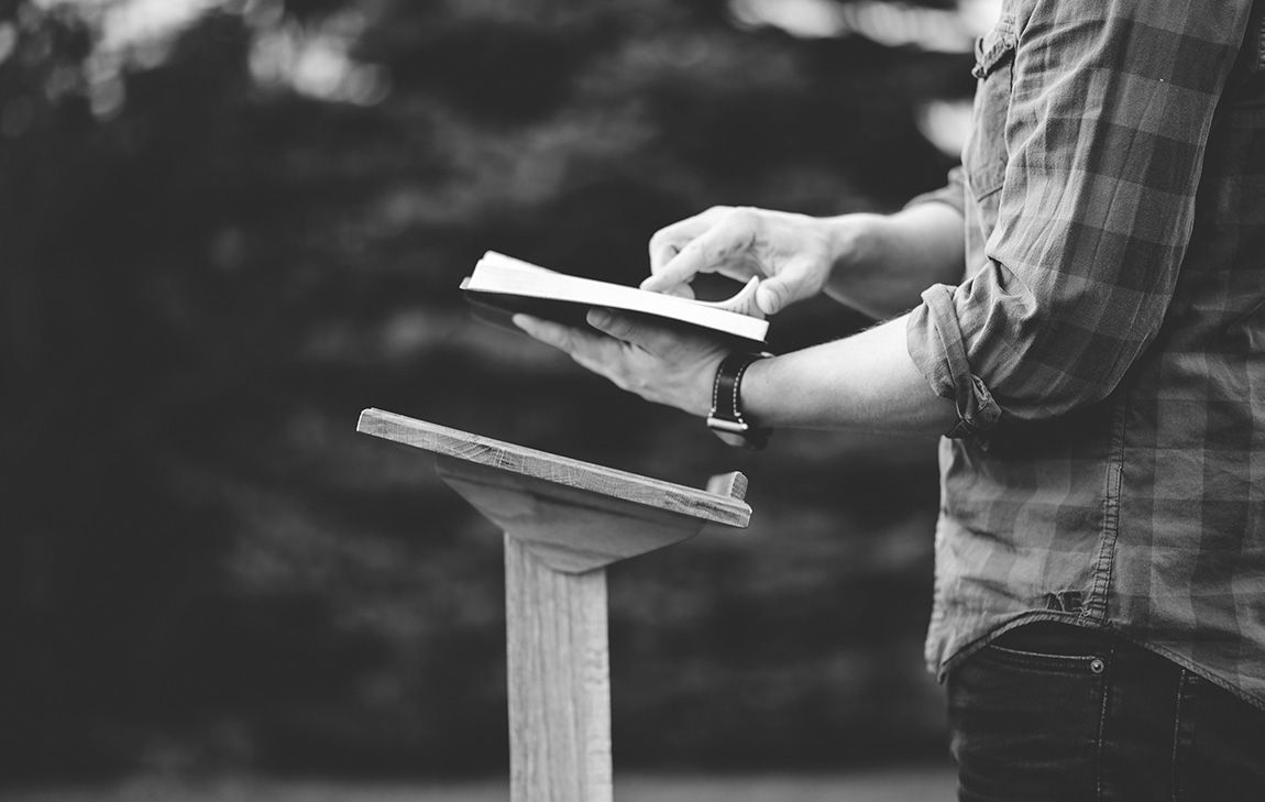 Man holding a book at an outdoor lectern, symbolizing a secular funeral celebrant leading a personalized, non-religious memorial service.