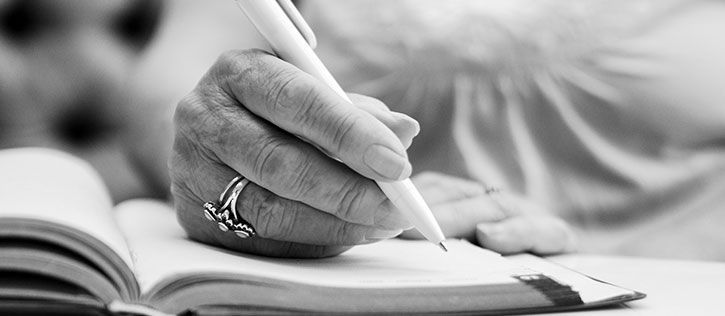 Close-up of a hand writing in a planner or journal with a pen, symbolizing thoughtful preparation and preplanning of funeral services.
