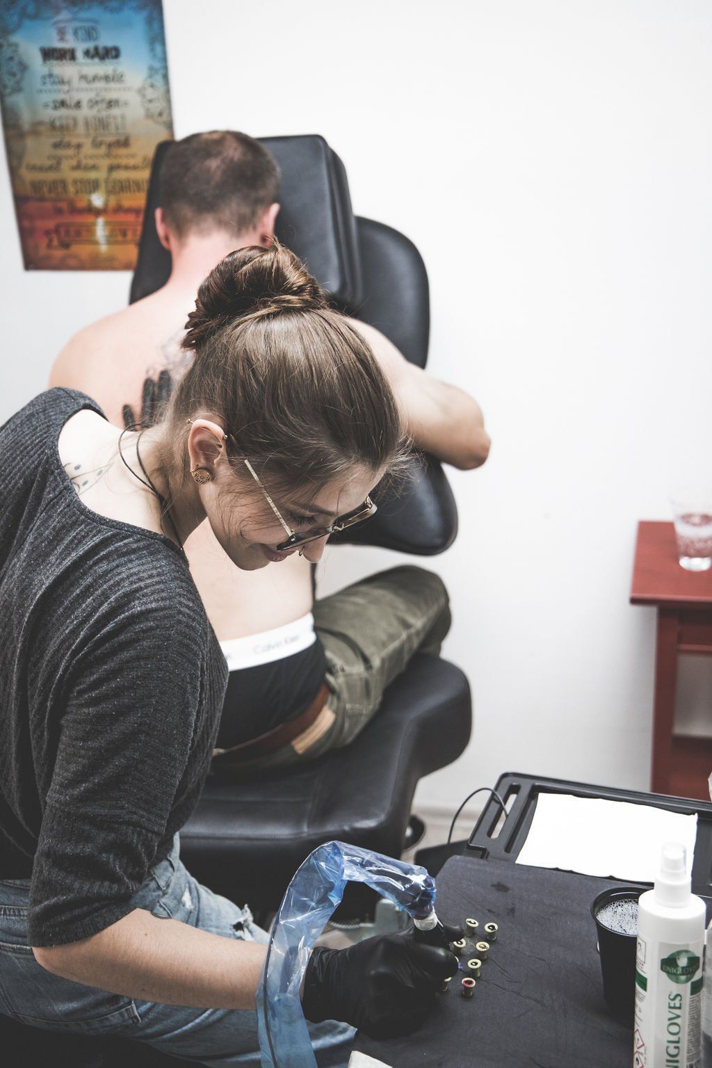 Eine Person tätowiert einem Kunden in einem Tattoo-Studio den Rücken; der Tätowierer konzentriert sich auf seine Arbeit.