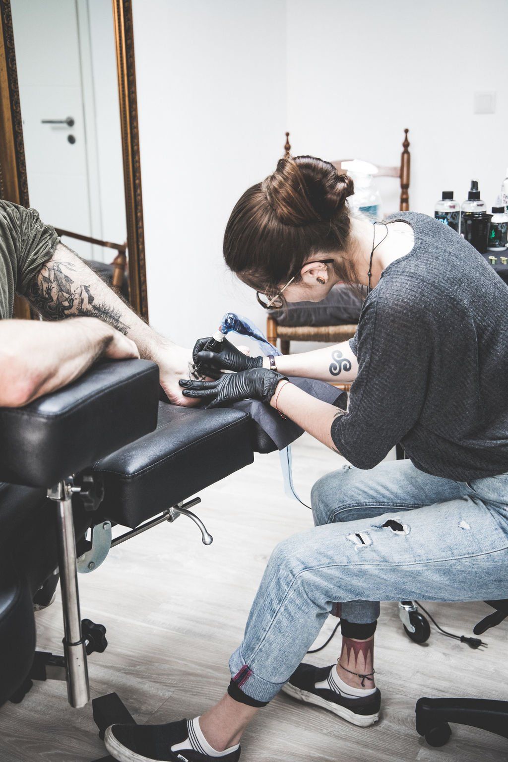 Tätowierer arbeitet an einem Arm eines Kunden; benutzt eine Maschine, in einem Tattoo-Studio.