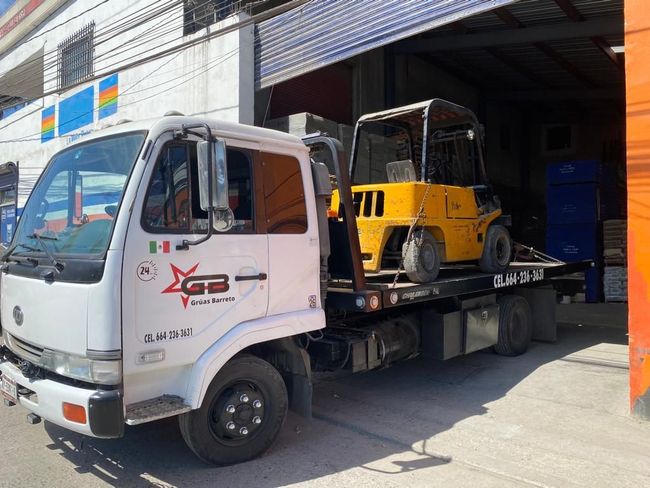 Una grúa blanca con un montacargas amarillo en la parte trasera está estacionada frente a un edificio.