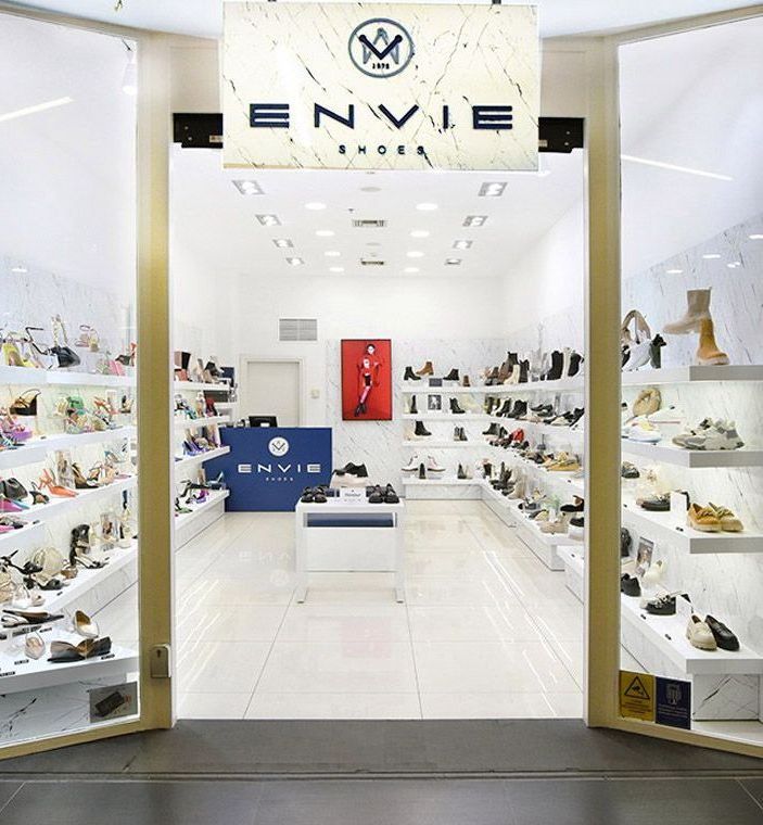 Exterior view of Envie Shoes store, displaying various shoes on shelves and a blue counter.