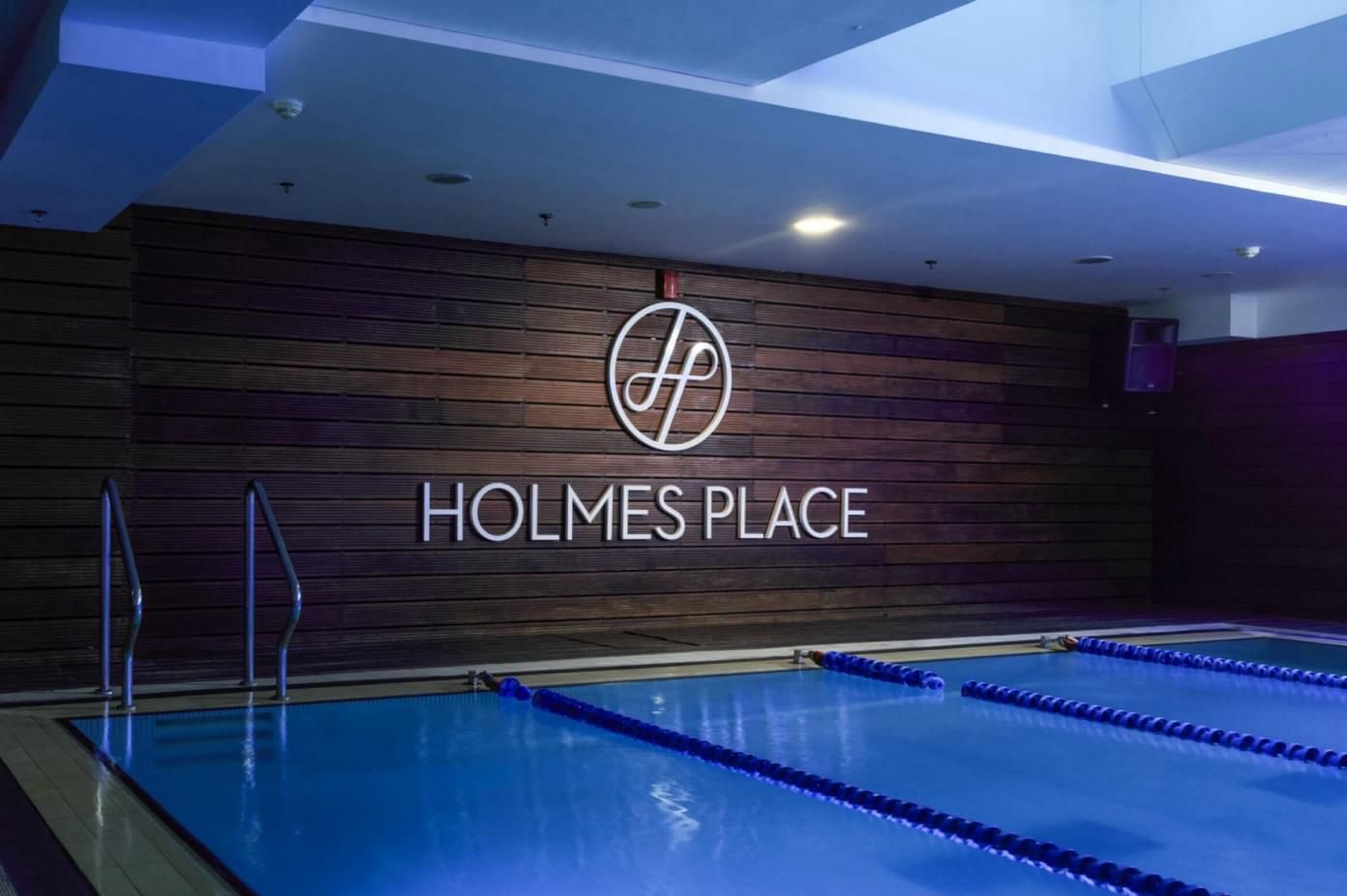 Swimming pool at Holmes Place gym, featuring the logo on a wooden wall. Blue water and lane lines.