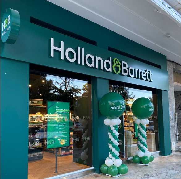Holland & Barrett store exterior, green and white sign, balloons, glass front, health store.