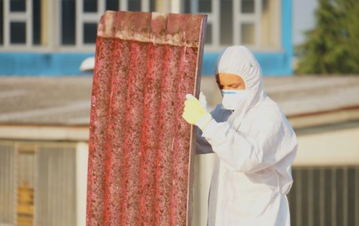 Persona in tuta protettiva che tiene in mano un pannello ondulato rosso. Edificio sullo sfondo.