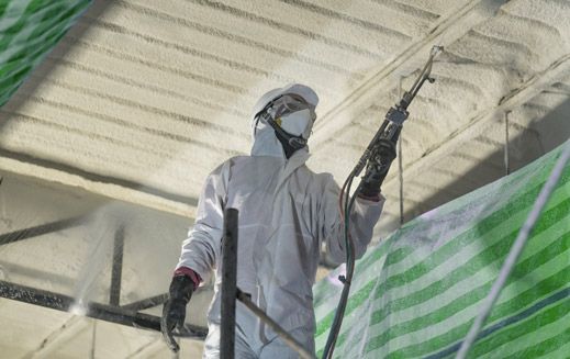 Un operaio in tuta protettiva spruzza un isolante sul soffitto.