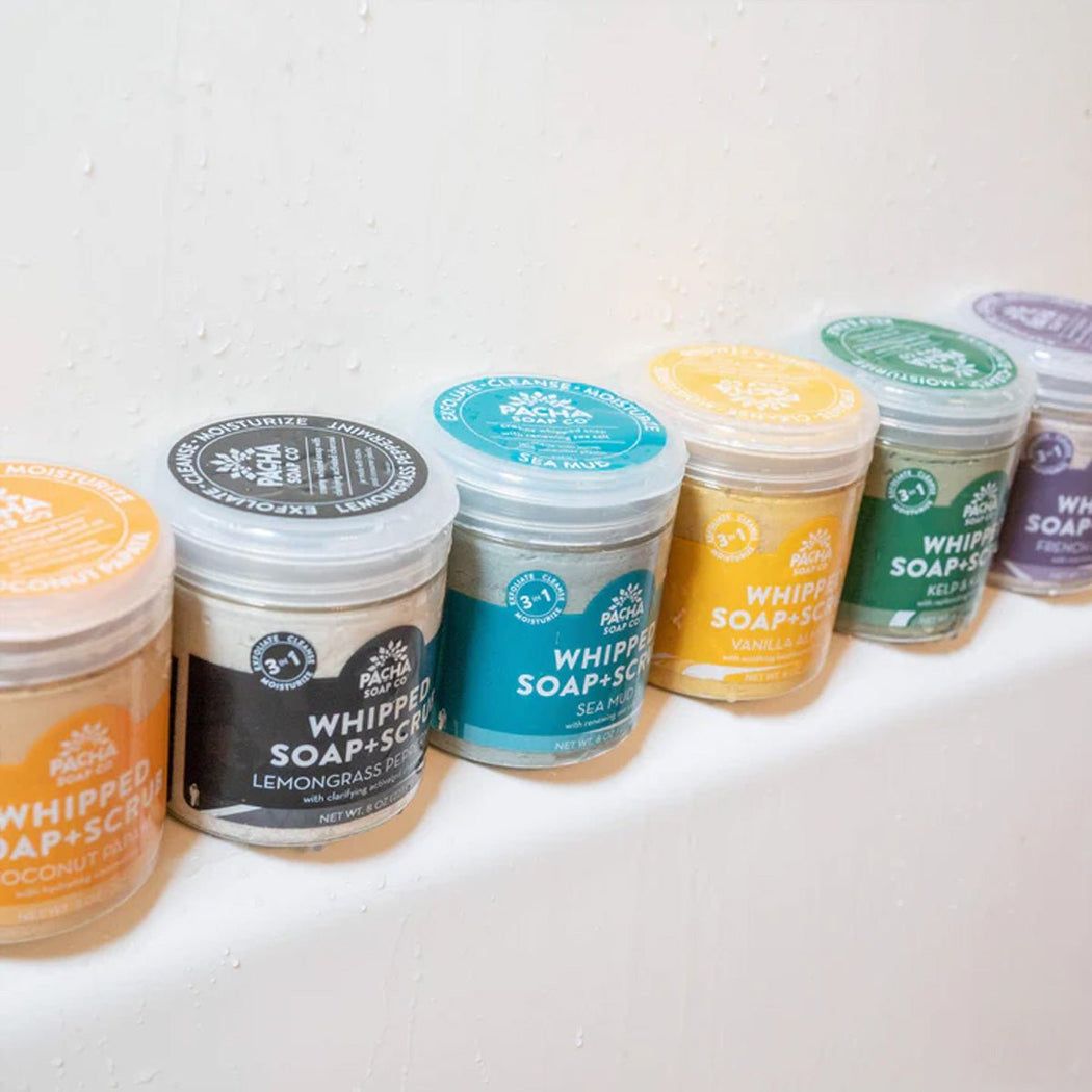 A row of jars of whipped soap with labels are lined up on a counter.