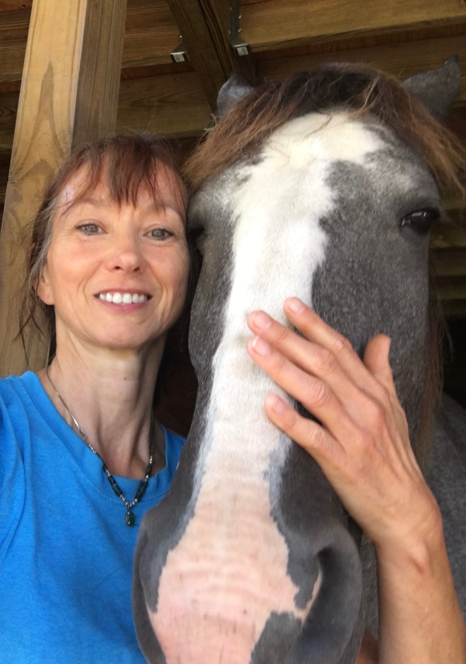 A woman is petting a horse in a stable.