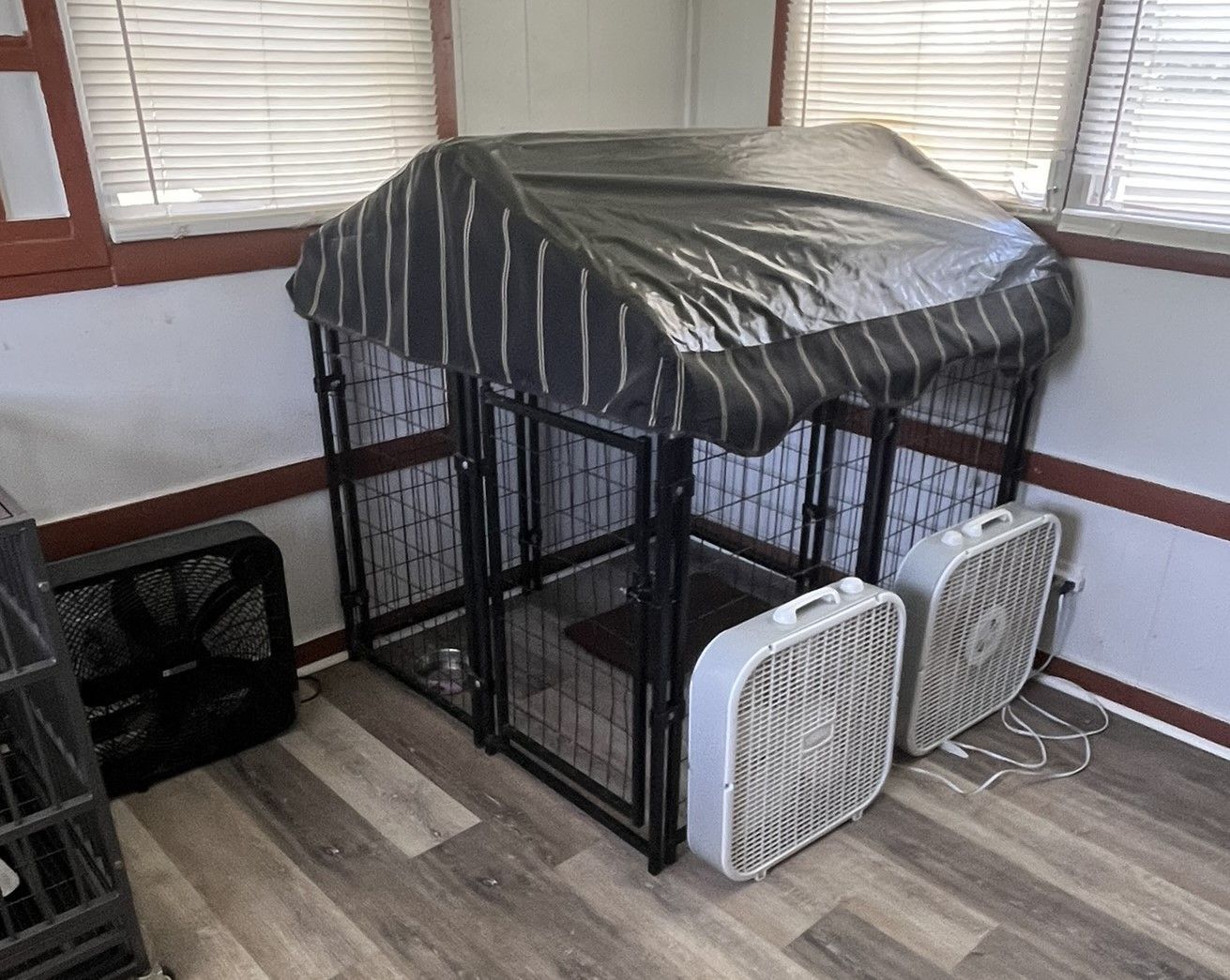 A dog cage with a canopy and two fans in a room.