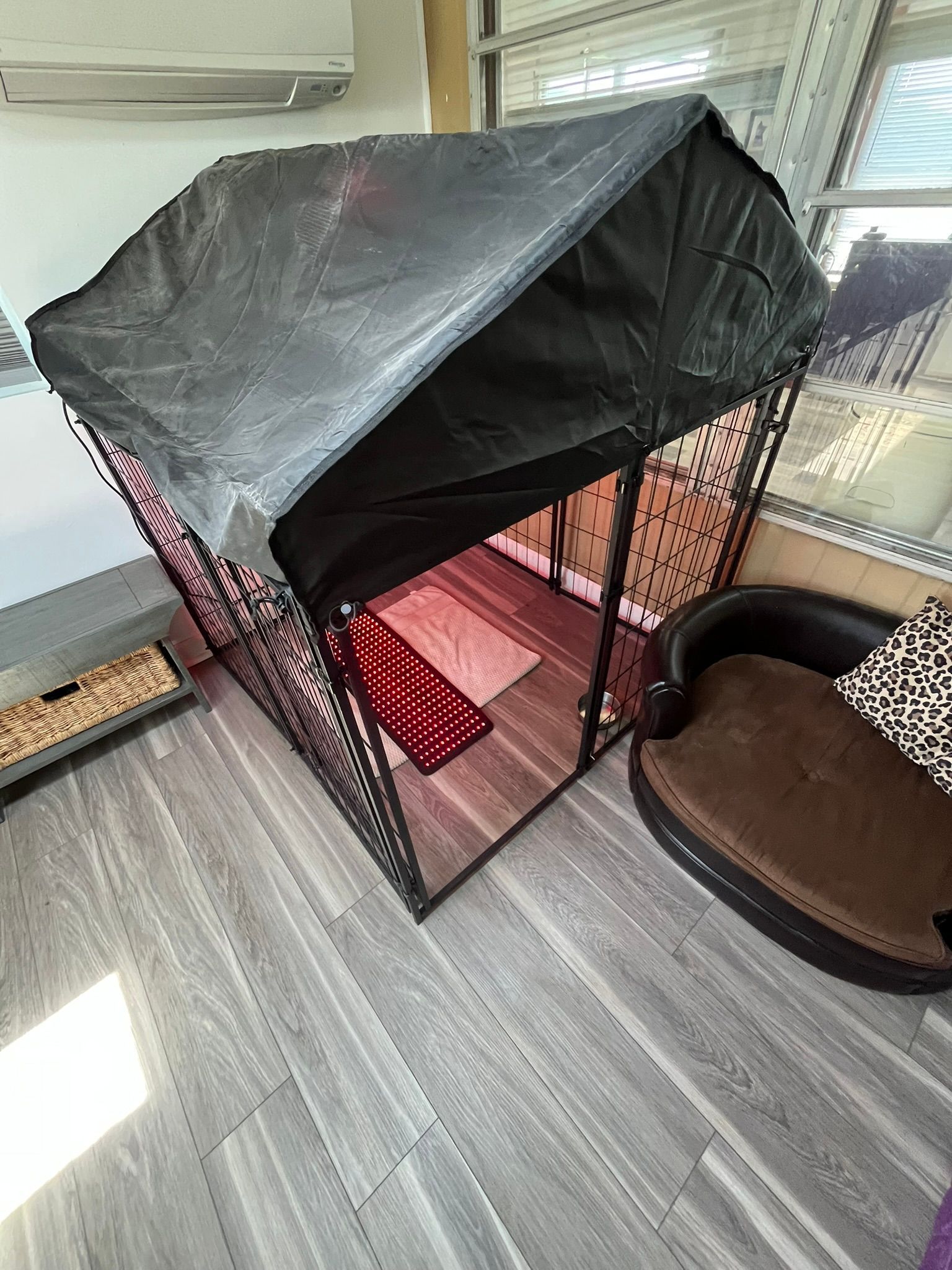 A dog cage with a roof is sitting on a wooden floor next to a dog bed.
