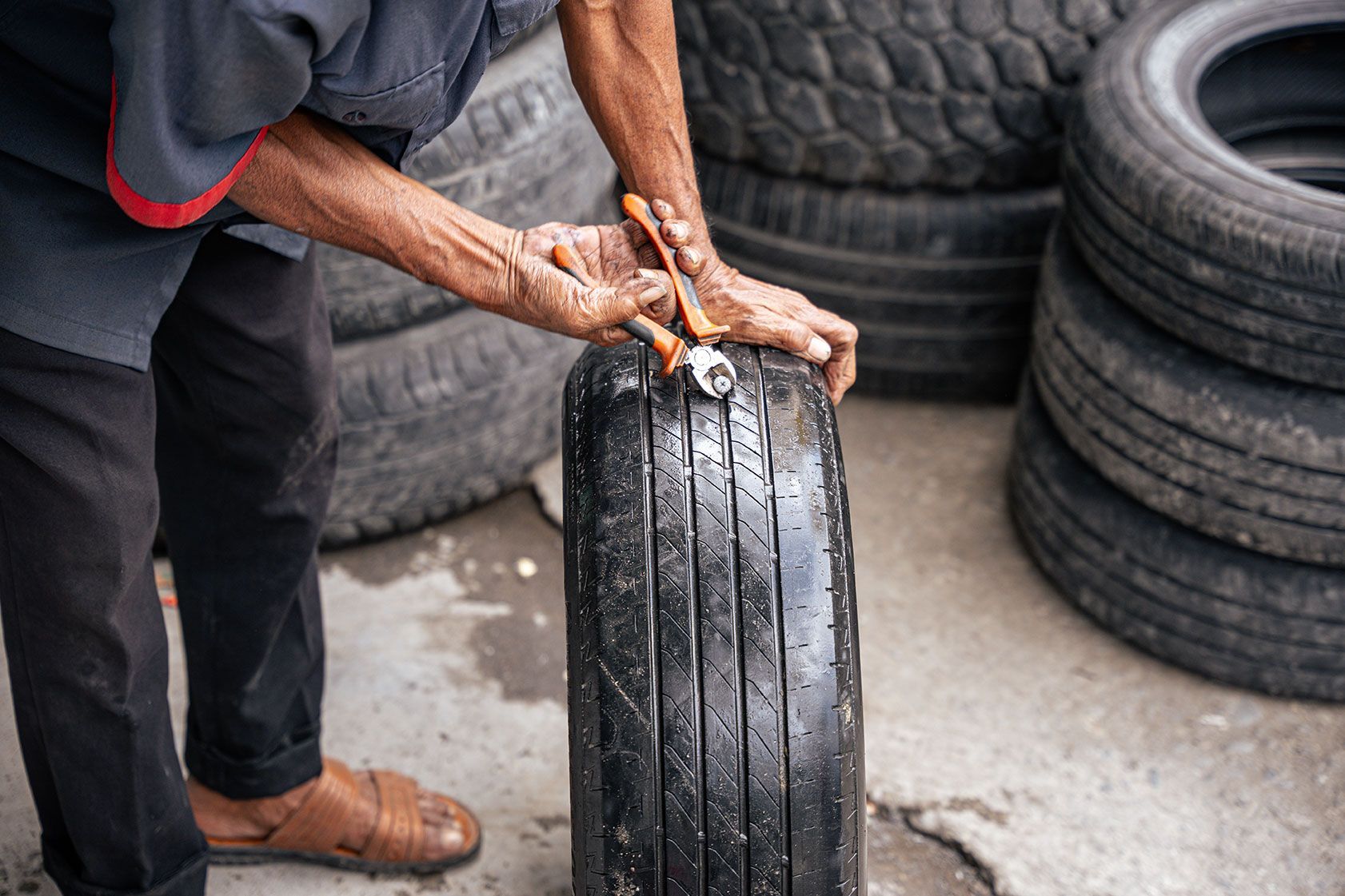 Person repairing a tire with tools; tires stacked in the background.