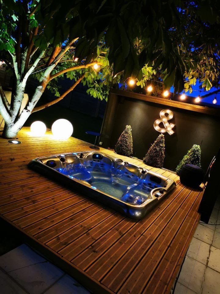 Un bain à remous est posé sur une terrasse en bois la nuit.