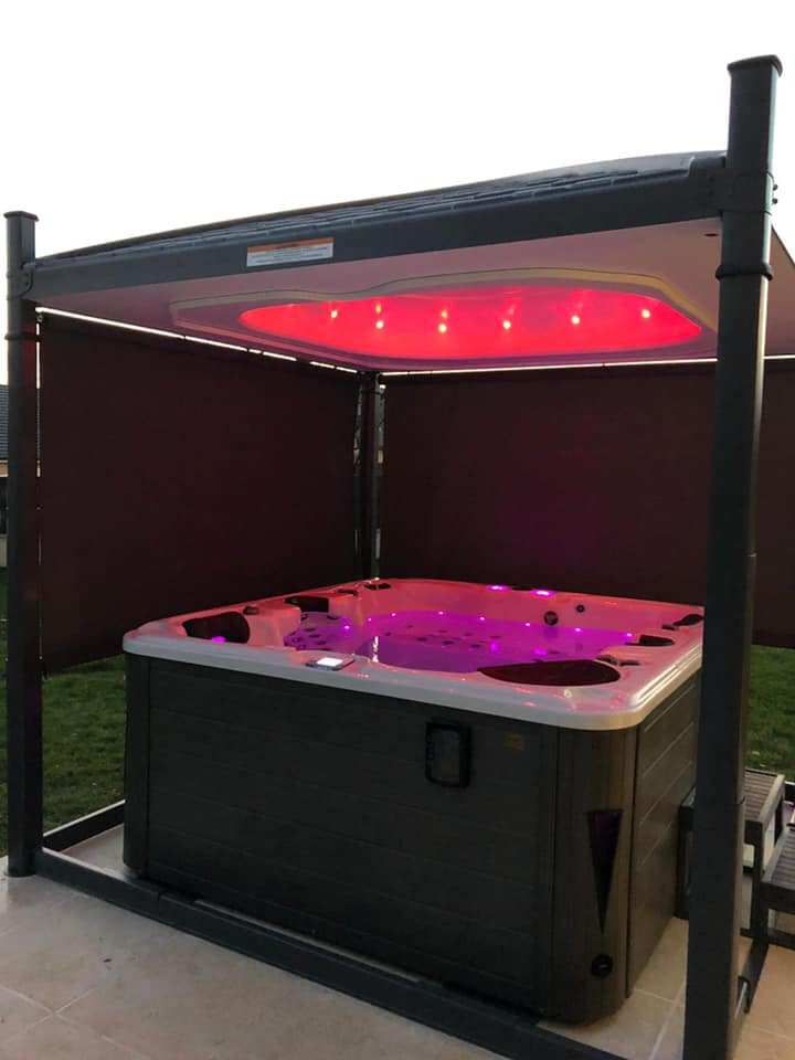 Un bain à remous est placé sous un auvent avec des lumières violettes.