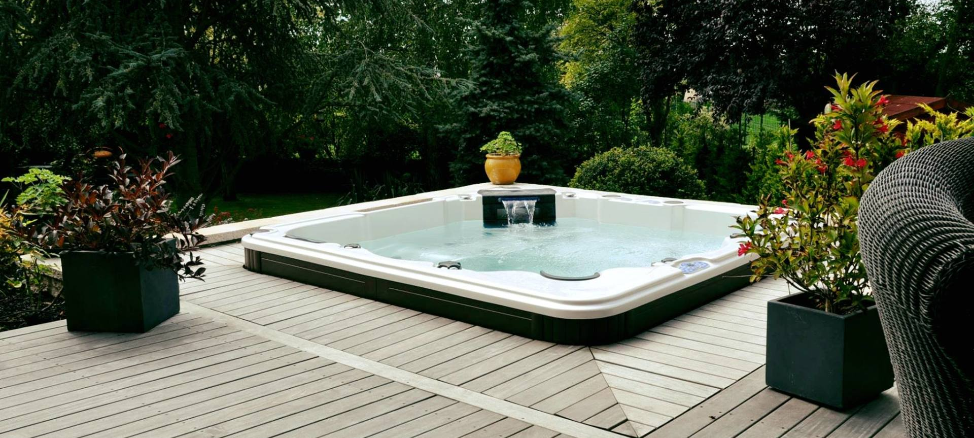 Un bain à remous est posé sur une terrasse en bois entourée d'arbres.