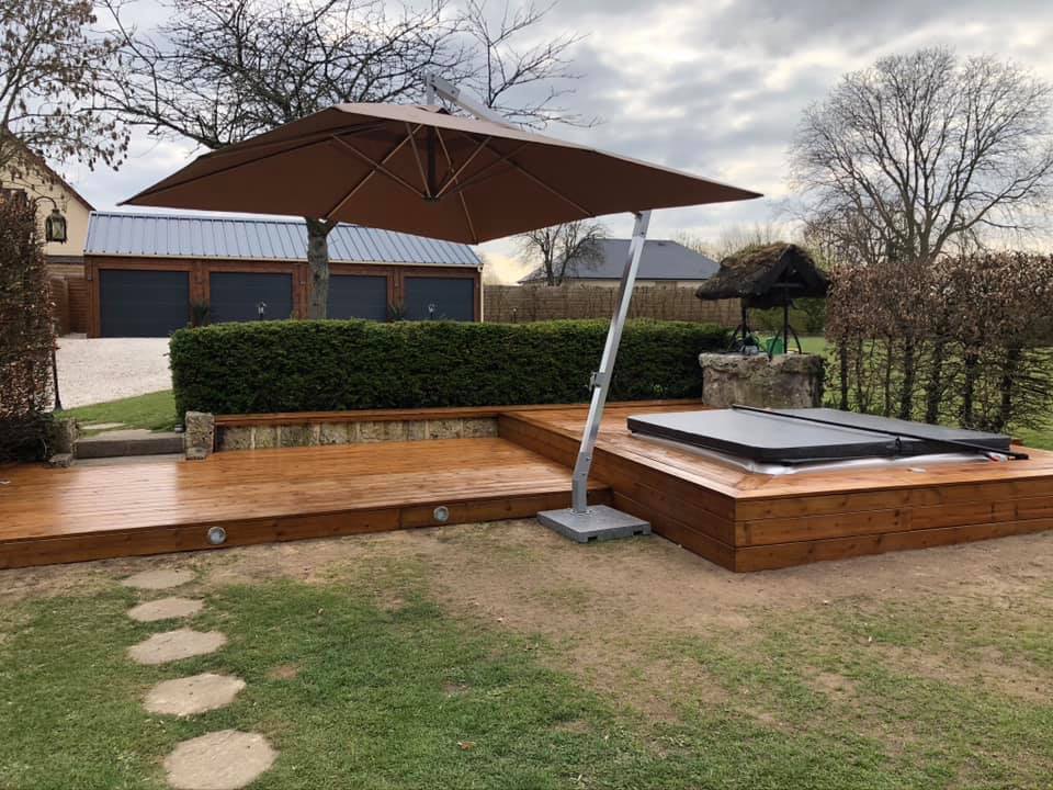 Un grand parasol est posé sur une terrasse en bois à côté d'un bain à remous.