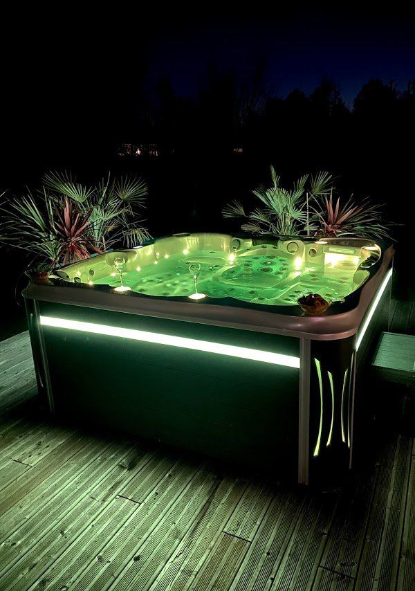 Un bain à remous est éclairé la nuit sur une terrasse en bois.
