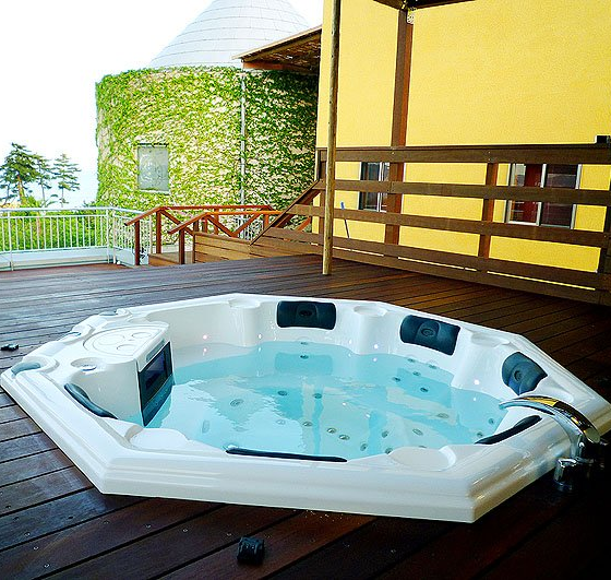 Un jacuzzi sur une terrasse avec un bâtiment jaune en arrière-plan
