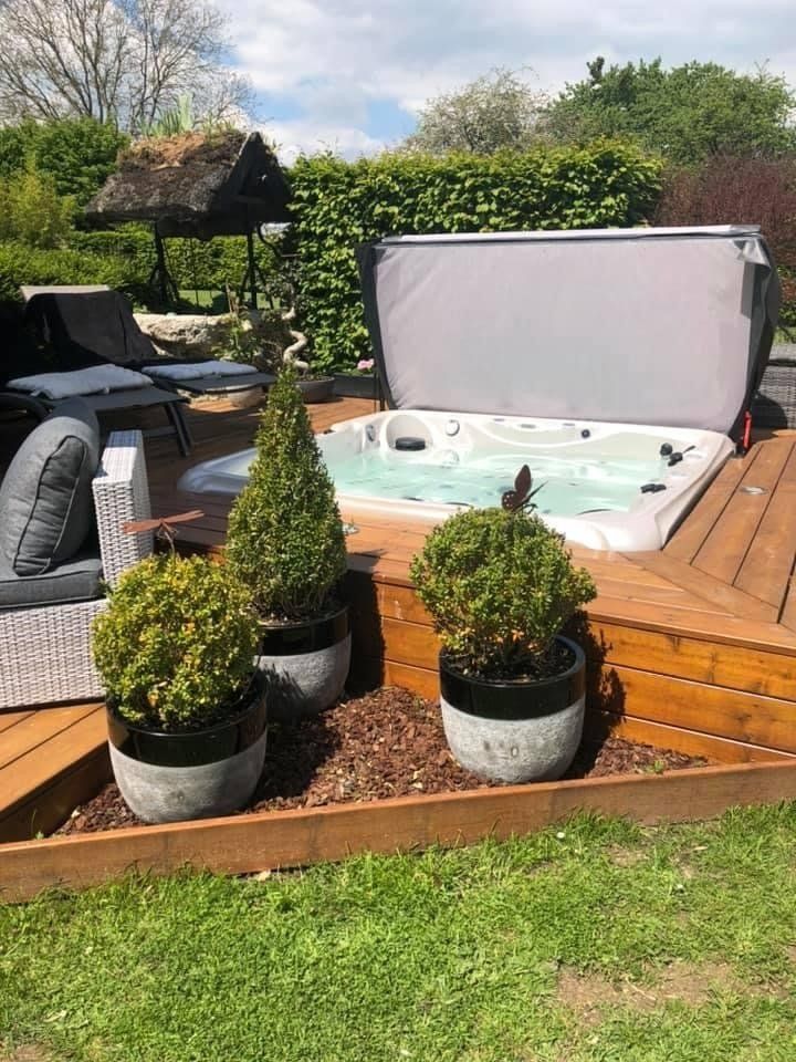 Un bain à remous est posé sur une terrasse en bois entourée de plantes en pot.