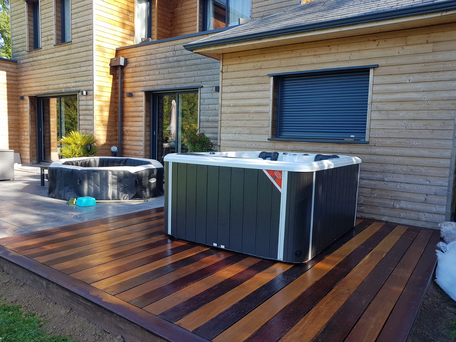 Un bain à remous est installé sur une terrasse en bois devant une maison.