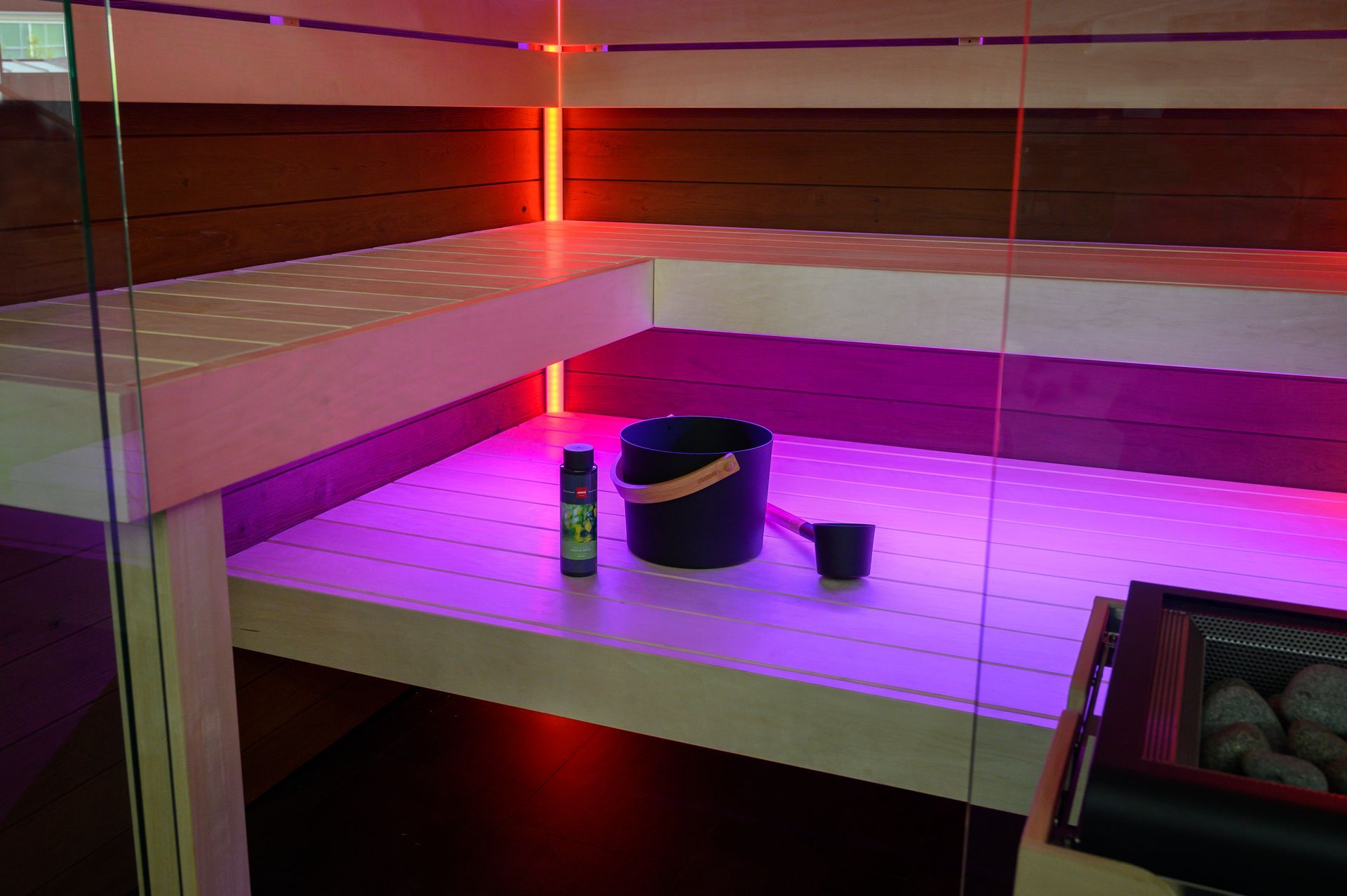 Un seau est posé sur une étagère dans un sauna avec des lumières violettes.