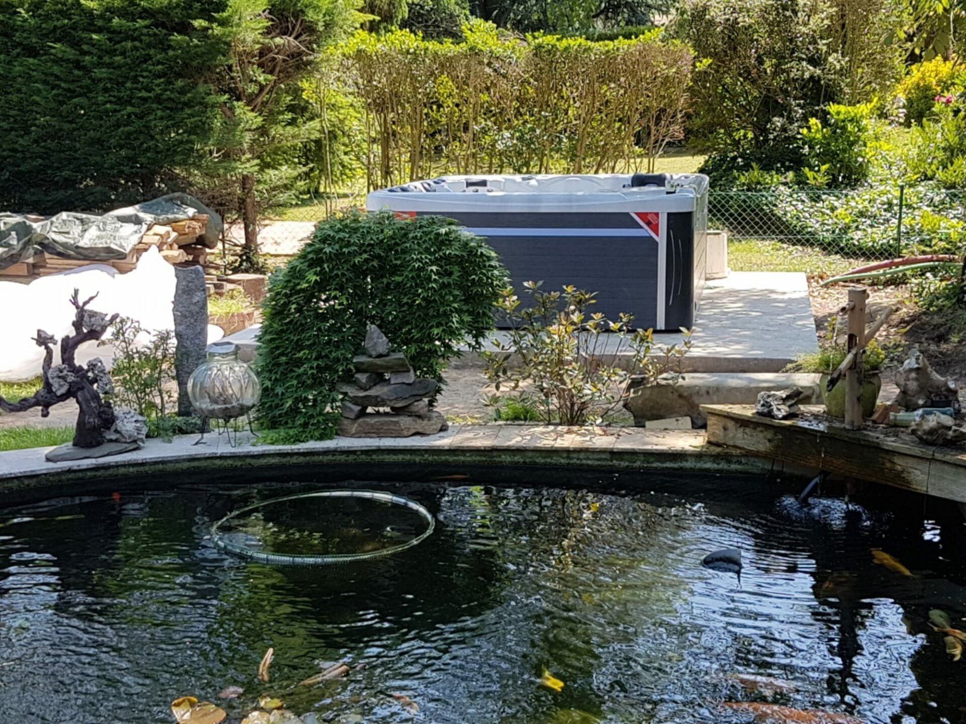 Un grand étang dans un jardin avec un bain à remous en arrière-plan.