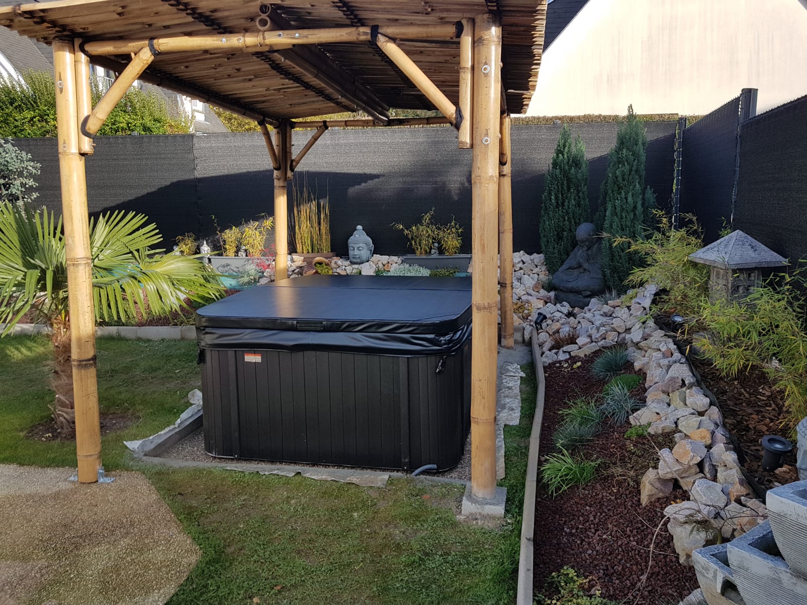 Un jacuzzi noir se trouve sous un gazebo en bambou dans un jardin.