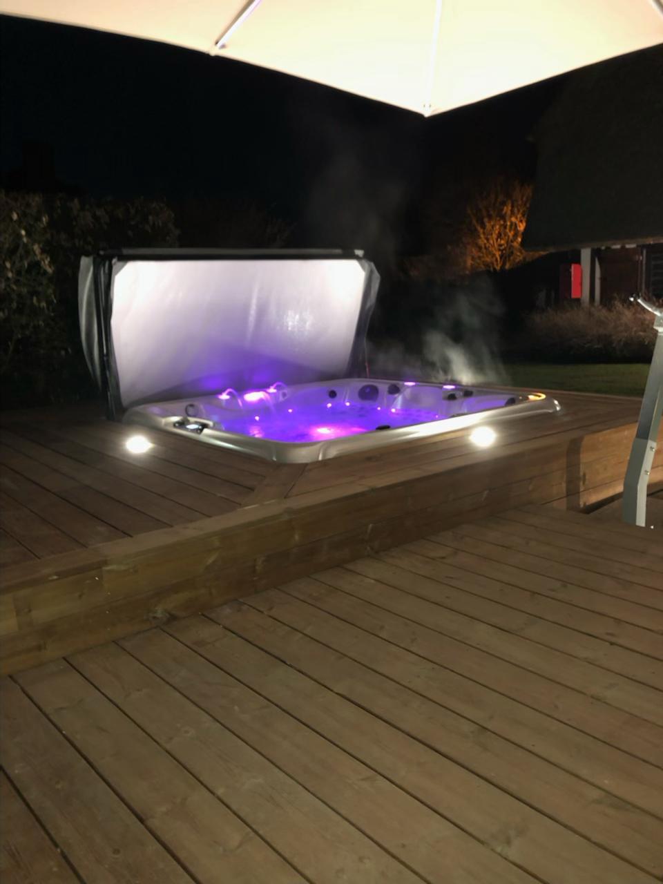 Un bain à remous est posé sur une terrasse en bois la nuit.