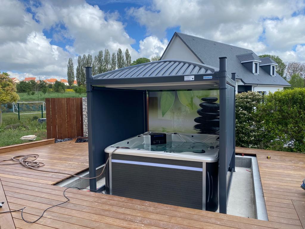 Un bain à remous est installé sous un auvent sur une terrasse devant une maison.