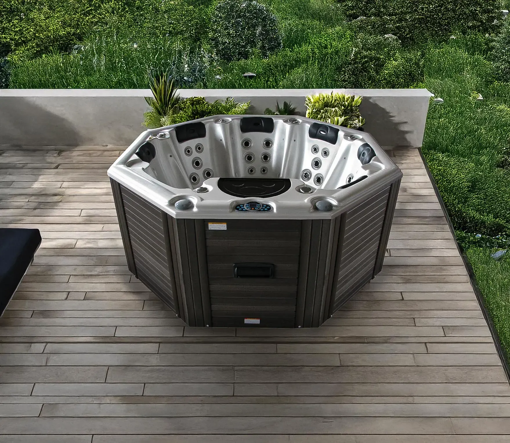 Un spa hexagonal avec des panneaux gris et marron se trouve sur une terrasse en bois, à côté d'une zone herbeuse.