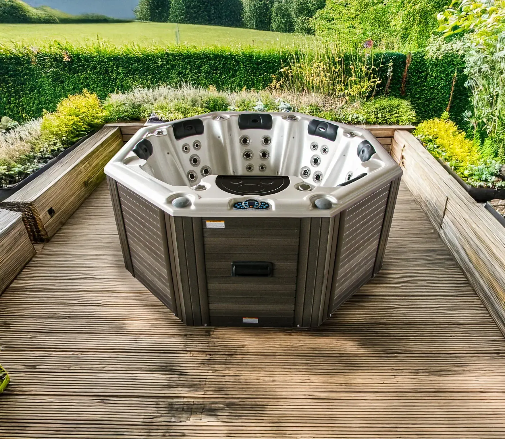 Un jacuzzi octogonal sur une terrasse en bois entourée de verdure. Gris et marron, il laisse apparaître les jets et le panneau de commande.