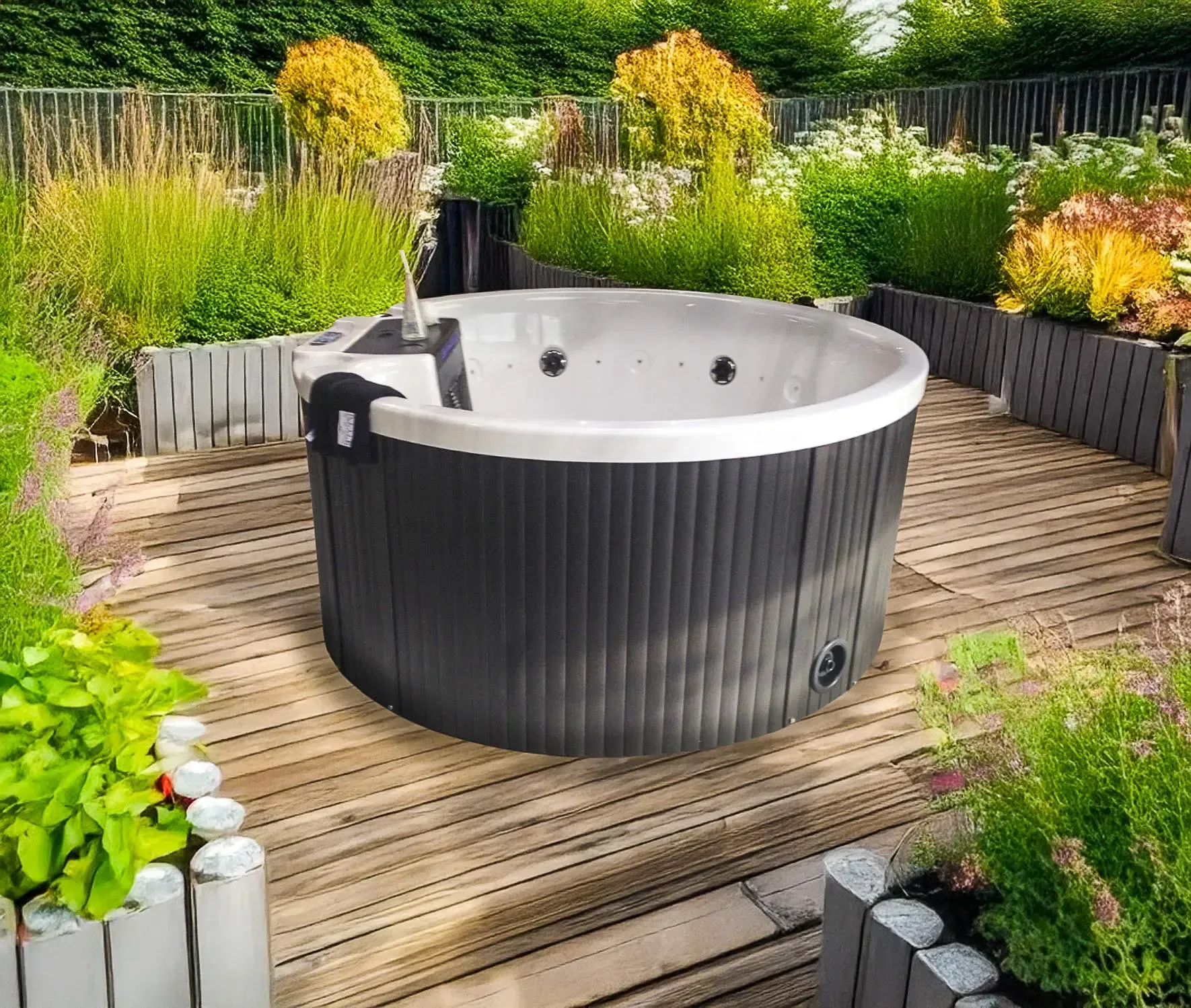 Spa rond sur une terrasse en bois entourée de plantes et de massifs de fleurs. Extérieur sombre et intérieur blanc.