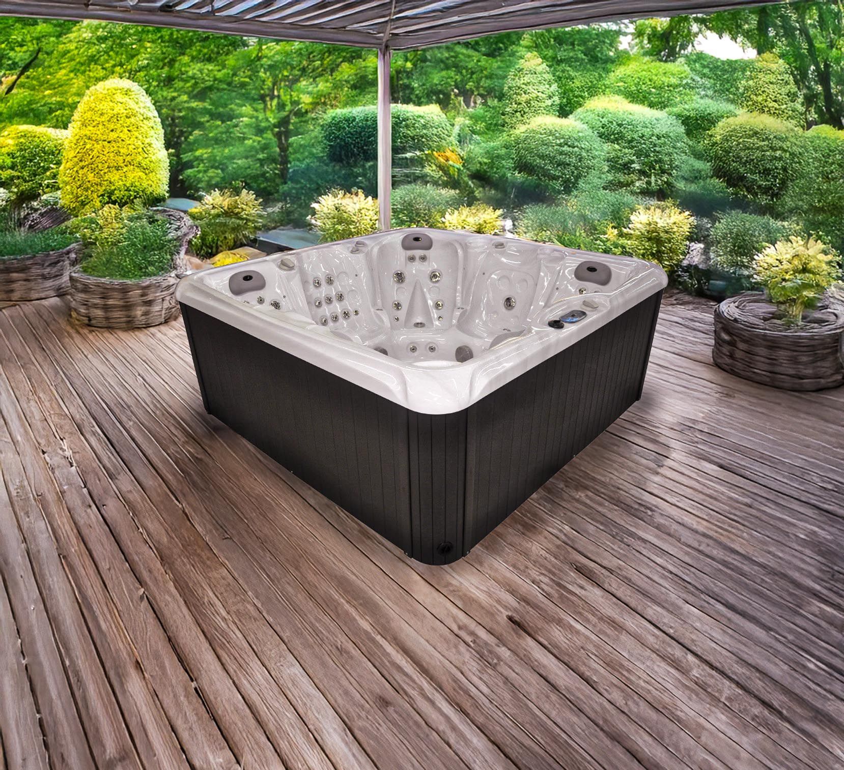 Un jacuzzi est installé sur une terrasse en bois sous une pergola, entouré d'une végétation luxuriante dans un cadre de jardin.
