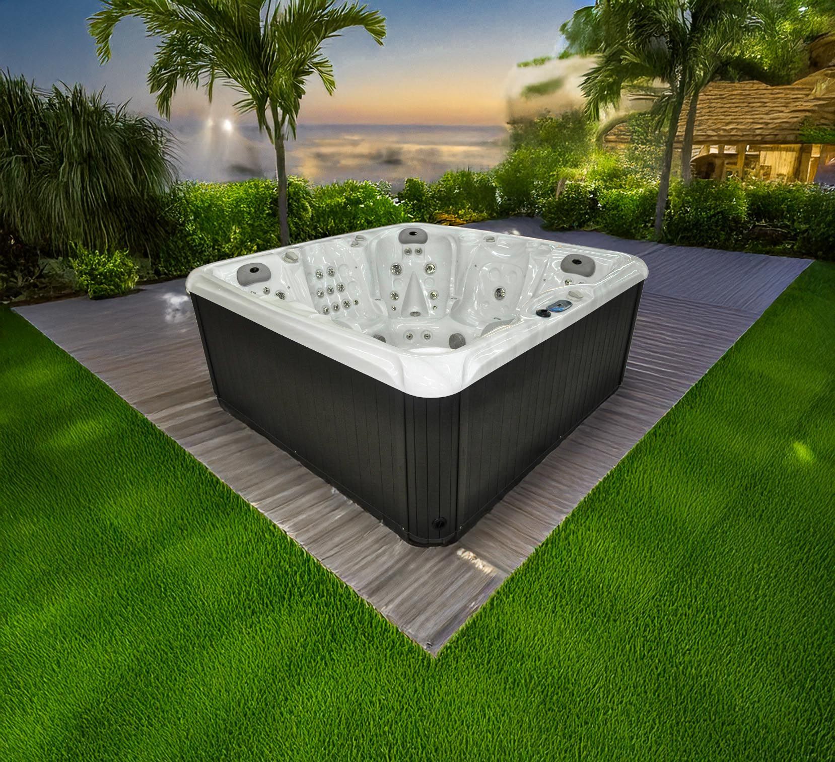 Un jacuzzi carré sur une terrasse dans une cour herbeuse avec des palmiers et un coucher de soleil en arrière-plan.
